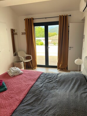 Une chambre à coucher comprenant un lit, une chaise, une petite table et une vue sur l’extérieur grâce à une porte coulissante.