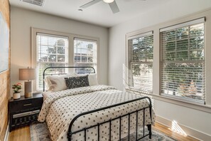A bedroom with a bed, a nightstand, a lamp, and large windows with blinds. - Walk to Downtown Tyler! Updated Historic Apt (Tyler)
