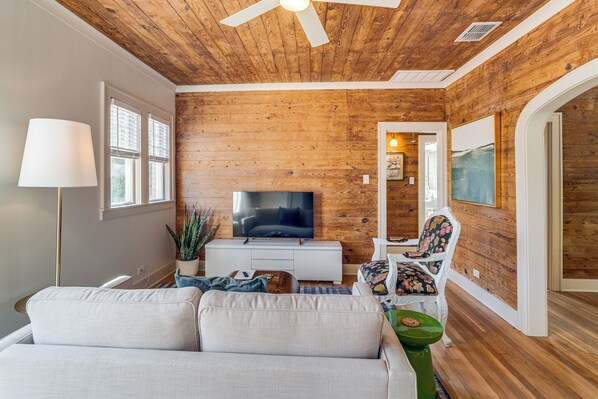 A living room with a wooden ceiling, a flat-screen TV, a sofa, a chair, and a side table. - Walk to Downtown Tyler! Updated Historic Apt (Tyler)