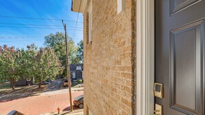 A residential building with a brick facade, a visible door with a keypad lock, and a street view with a parked car and trees. - Walk to Downtown Tyler! Updated Historic Apt (Tyler)