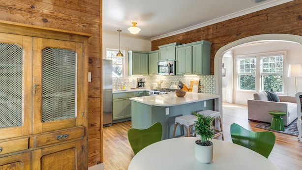 A kitchen with wooden cabinets, a central island, and a dining area with chairs. - Walk to Downtown Tyler! Updated Historic Apt (Tyler)
