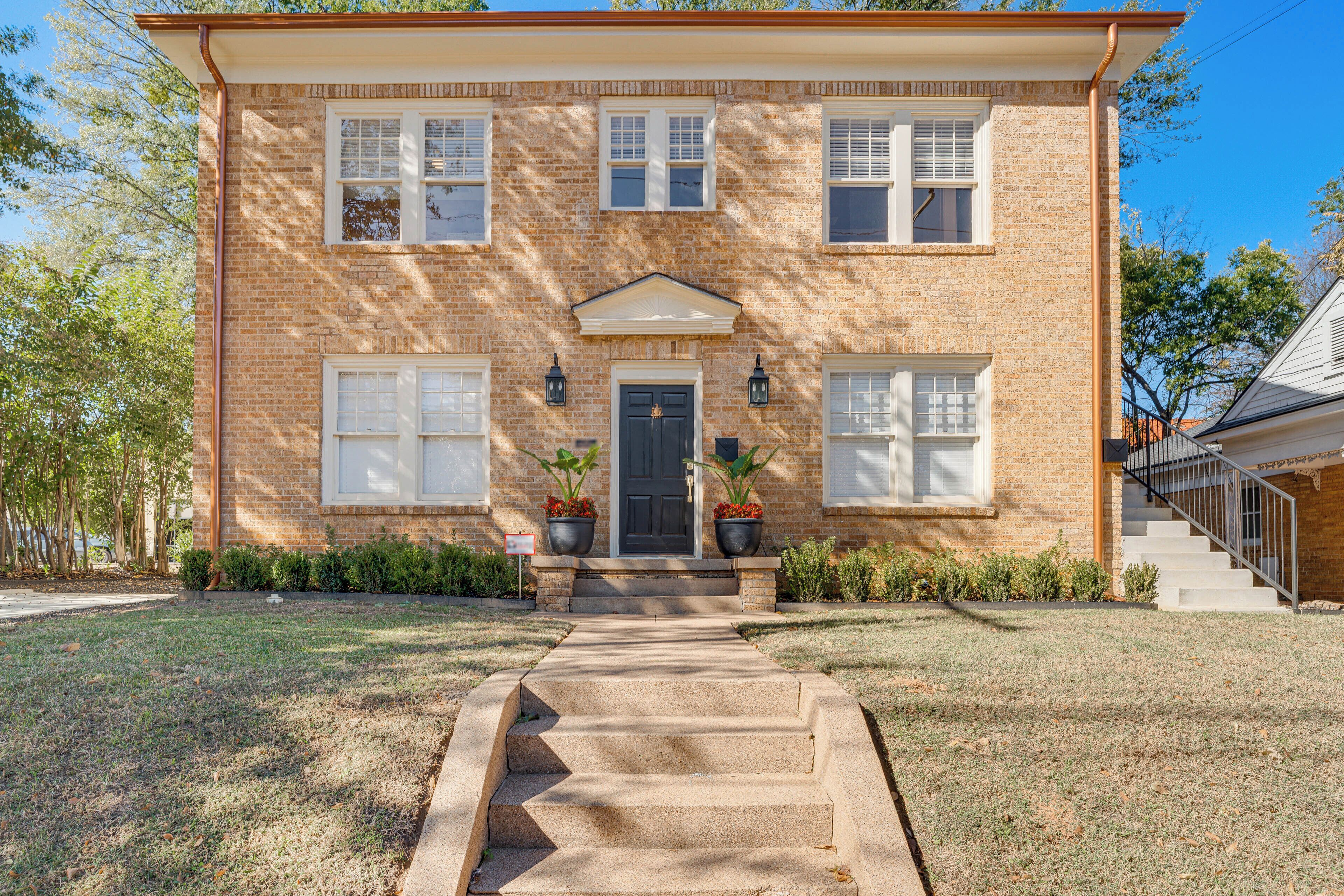 A two-story brick house with a front porch, a central entrance, and a staircase leading to the front door.