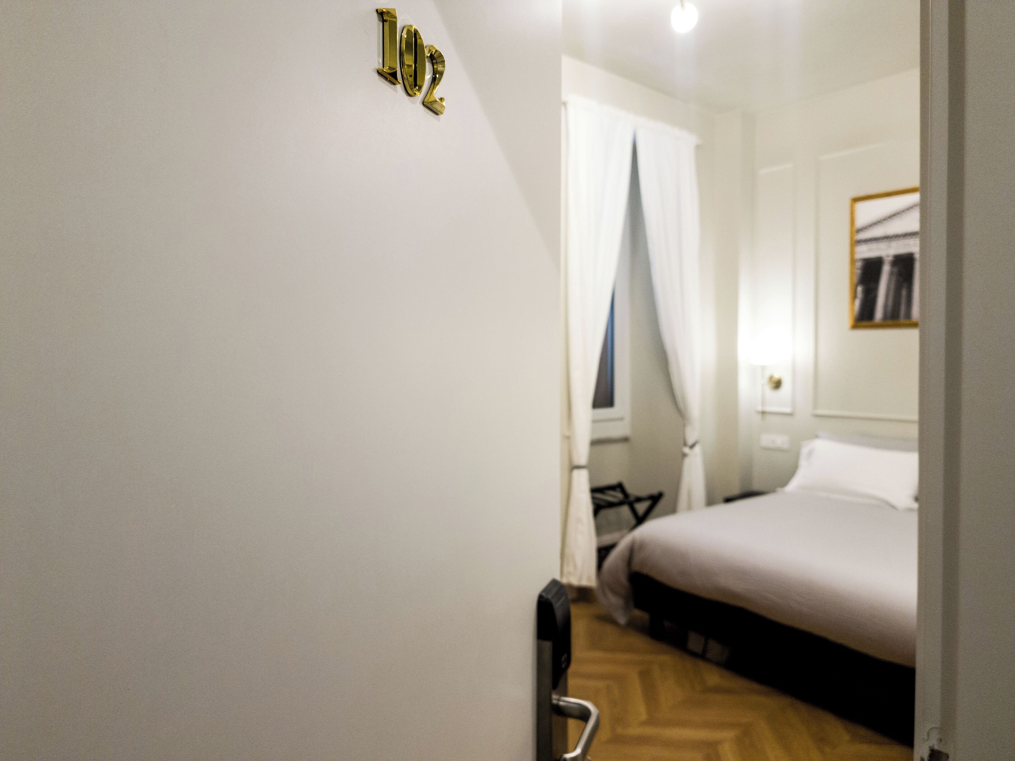 Et hotelværelse med en seng, en dør med håndtag og et nummer på væggen.