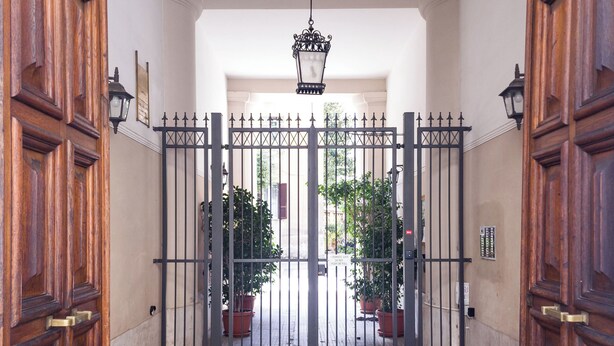 A gated entrance with a tiled floor, wooden doors, and potted plants. - Domus Innovatis Rooms & Home (Rome)