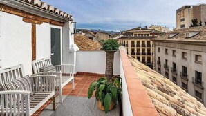 Una terraza en la azotea con un edificio blanco, una silla de madera y una planta en maceta.