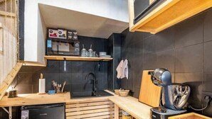 Una cocina compacta con un refrigerador negro, estantes de madera, un lavamanos y una cafetera.