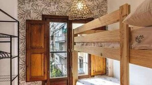 Una habitación con una cama litera, una puerta de madera, una ventana y un papel tapiz decorado.