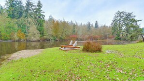 A lakeside park with a grassy area, a wooden bench, and a small fire pit. - Peaceful Patio View! Waterfront Puget Sound Unit (Poulsbo)