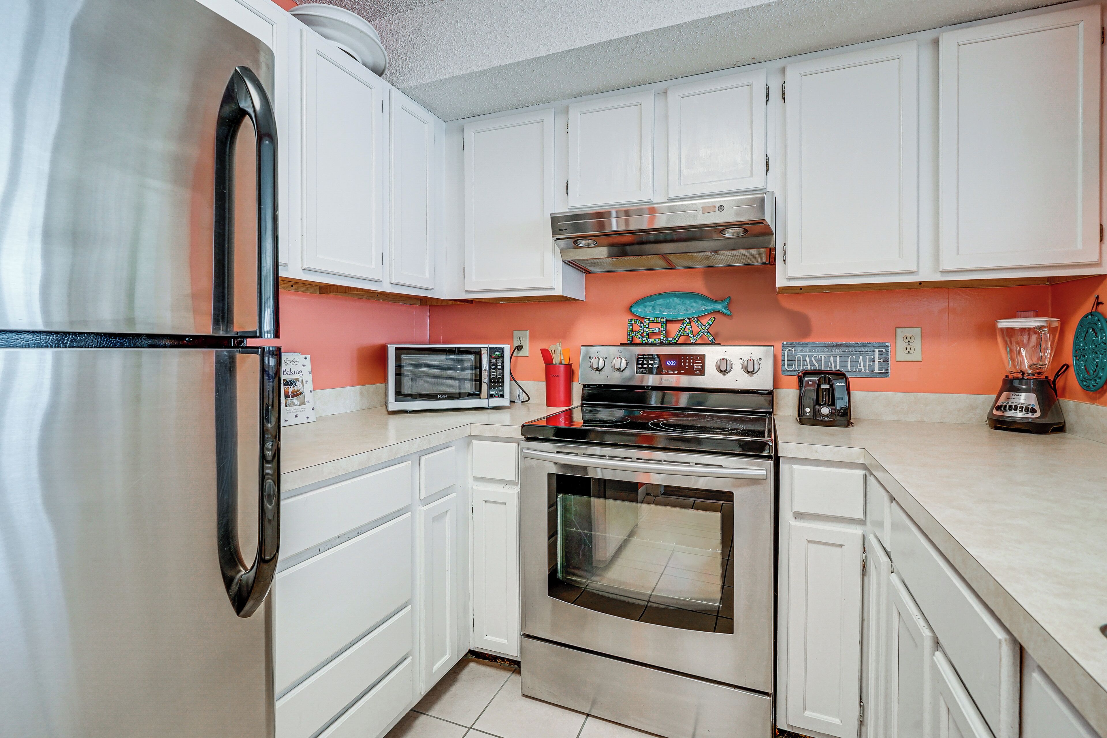 A kitchen with white cabinets, a stainless steel refrigerator, a microwave, an oven, and a toaster.
