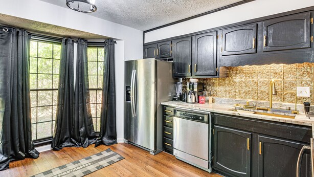Una cocina con gabinetes oscuros, un refrigerador de acero inoxidable, un lavavajillas y una ventana con cortinas negras.