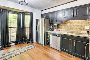 A kitchen with dark cabinets, a stainless steel refrigerator, a dishwasher, and a window with black curtains. - 6 Mi to Marietta Square: Family Retreat w/ Yard! (Marietta)