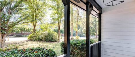 A covered porch with a view of a landscaped garden and trees.