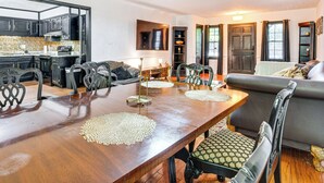 Amplia sala de estar con mesa de comedor de madera, sillas tapizadas y un sofá gris.