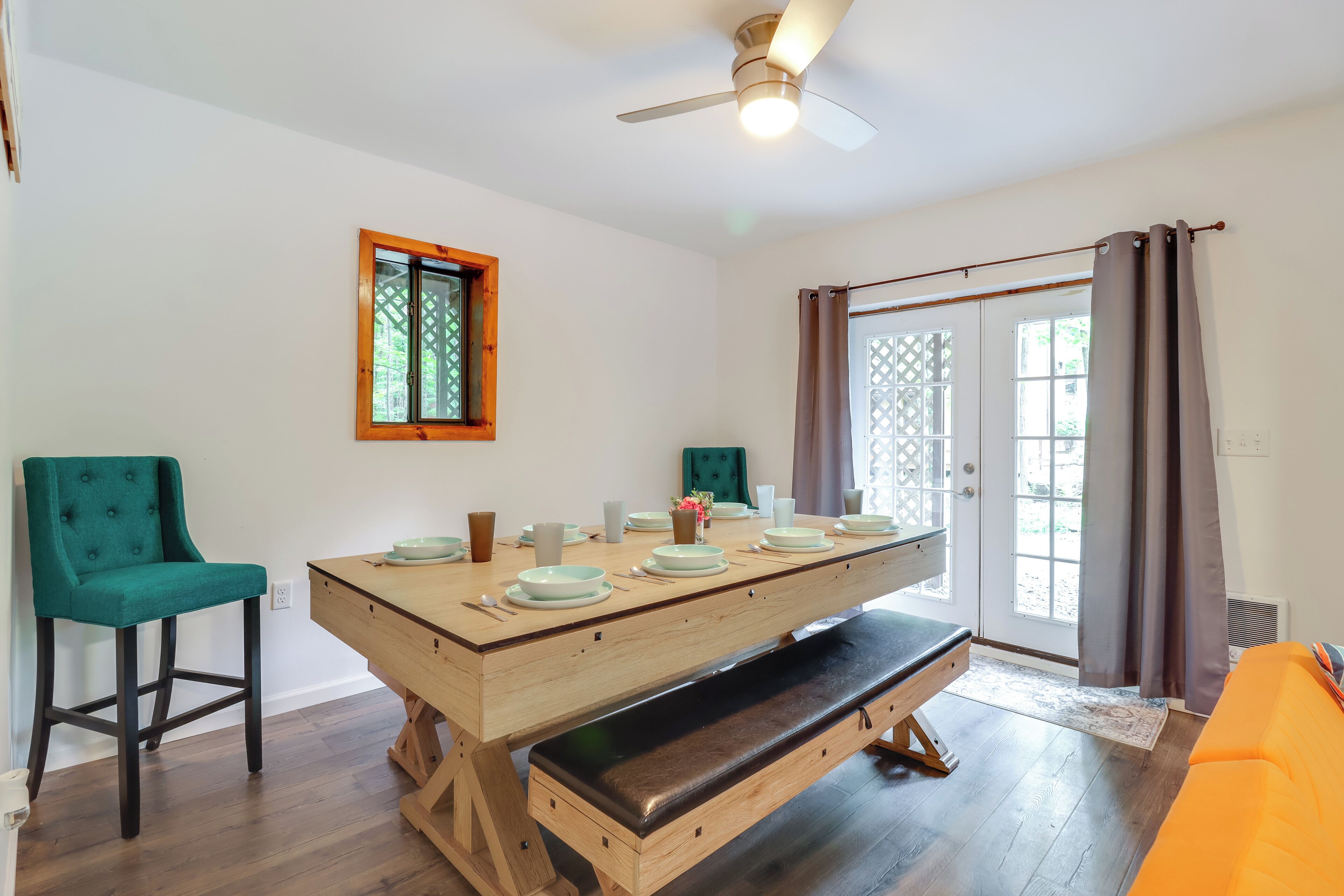 A dining area with a wooden table set for four, a bench, two chairs, and a ceiling fan.