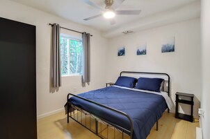 Un dormitorio con cama, ventilador de techo, ventana con cortinas y tres cuadros en la pared.