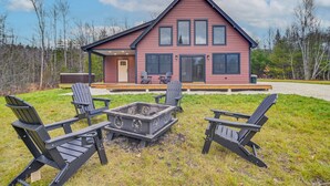 Ein zweistöckiges Haus mit einer Terrasse, einem Sitzbereich im Freien inklusive Adirondack-Stühlen und einer Feuerstelle.