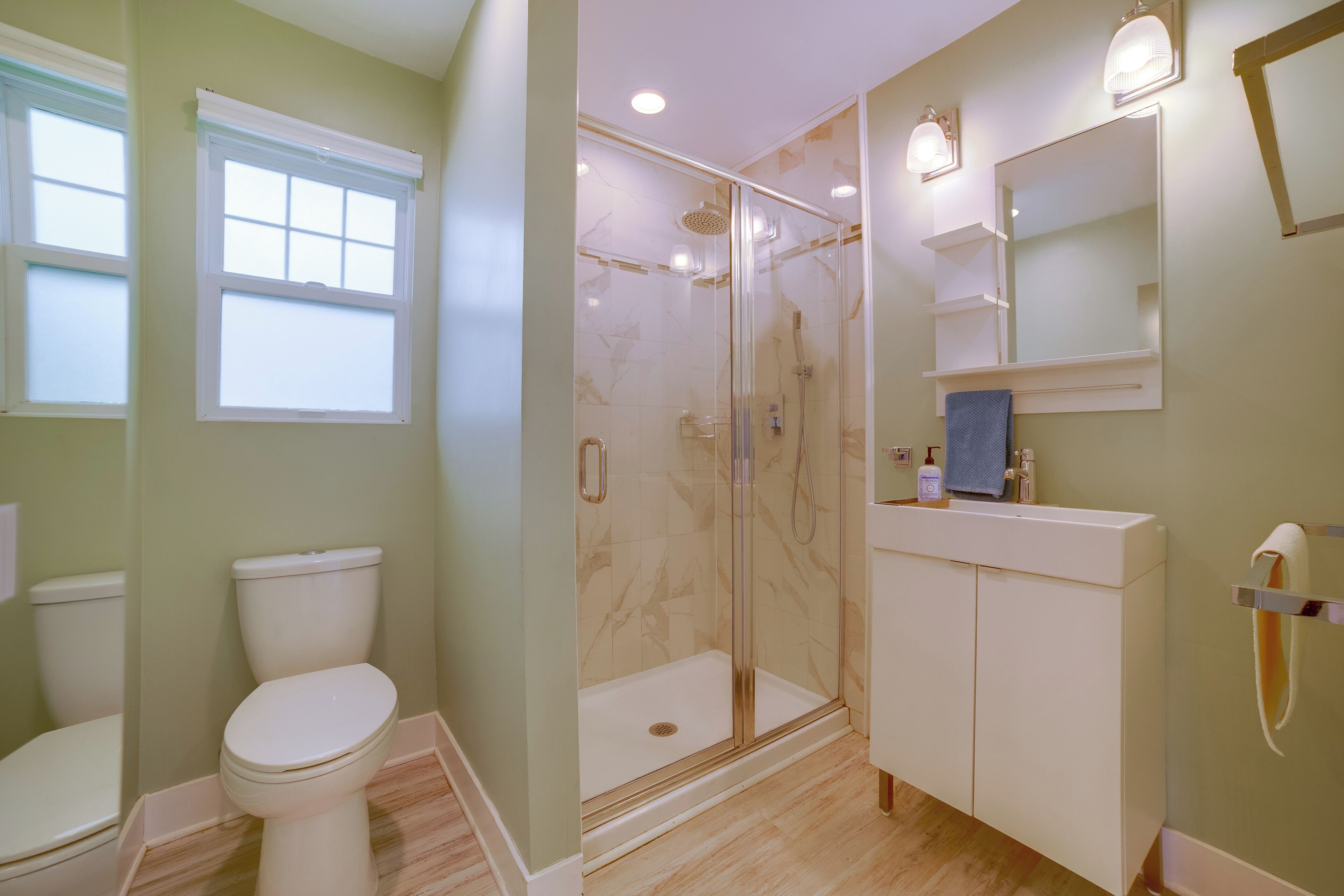 Une salle de bain comprenant des toilettes, une douche fermée par une paroi de verre, un lavabo et un miroir.