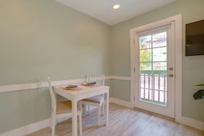 Una habitación con una mesa y sillas blancas, una puerta con ventana y una planta en la pared.