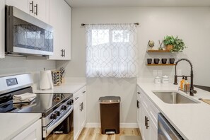 A modern kitchen with white cabinets, stainless steel appliances, a built-in oven, a sink, and a trash can. - Modern & Pet-friendly! Northern Colorado Retreat (Severance)