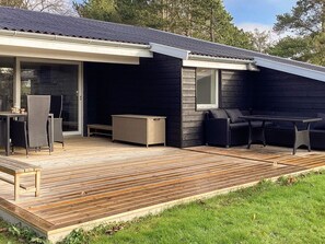 Eine moderne Terrass mit Holzboden, schwarzer Möbel und einer Glastür zu einem Innenraum.