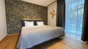 A bedroom with a large bed, a textured wall, and a window with curtains. - Gemmi Hotel & Spa (Kandersteg)
