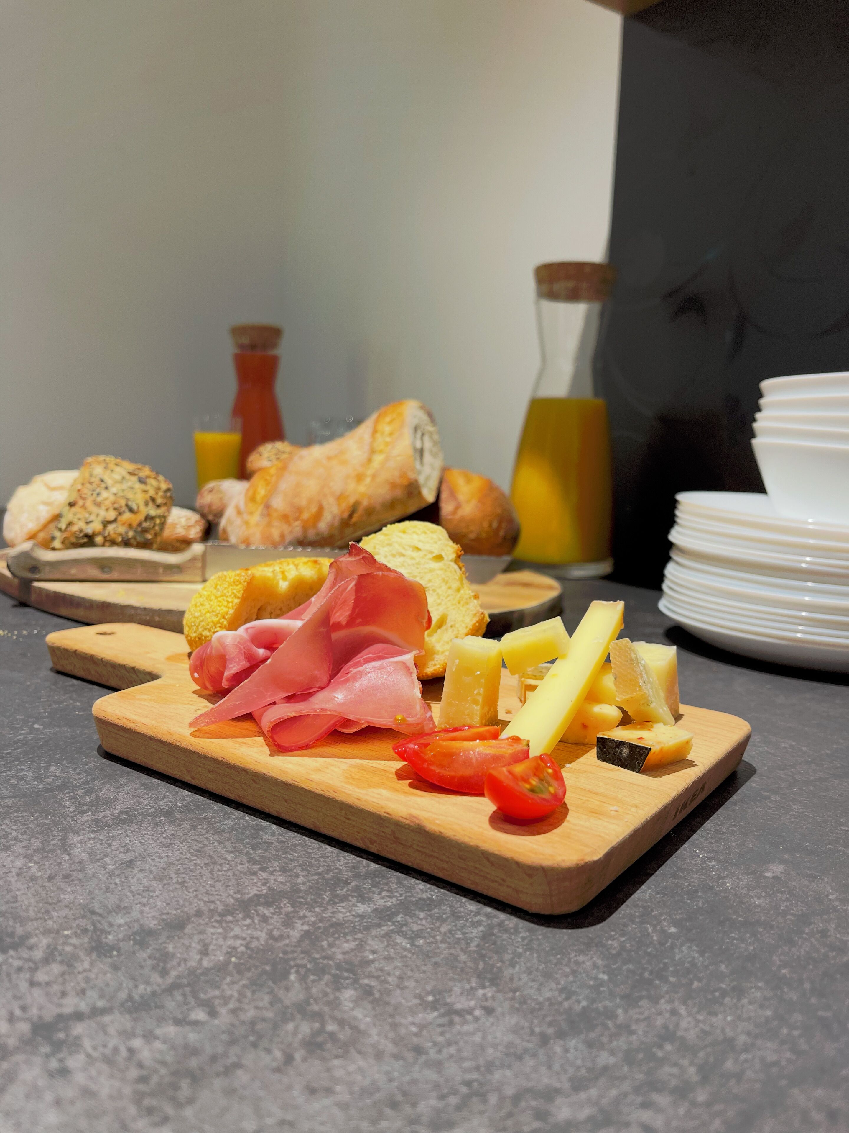 Una tabla de madera con diversos alimentos, como queso, jamón y pan.
