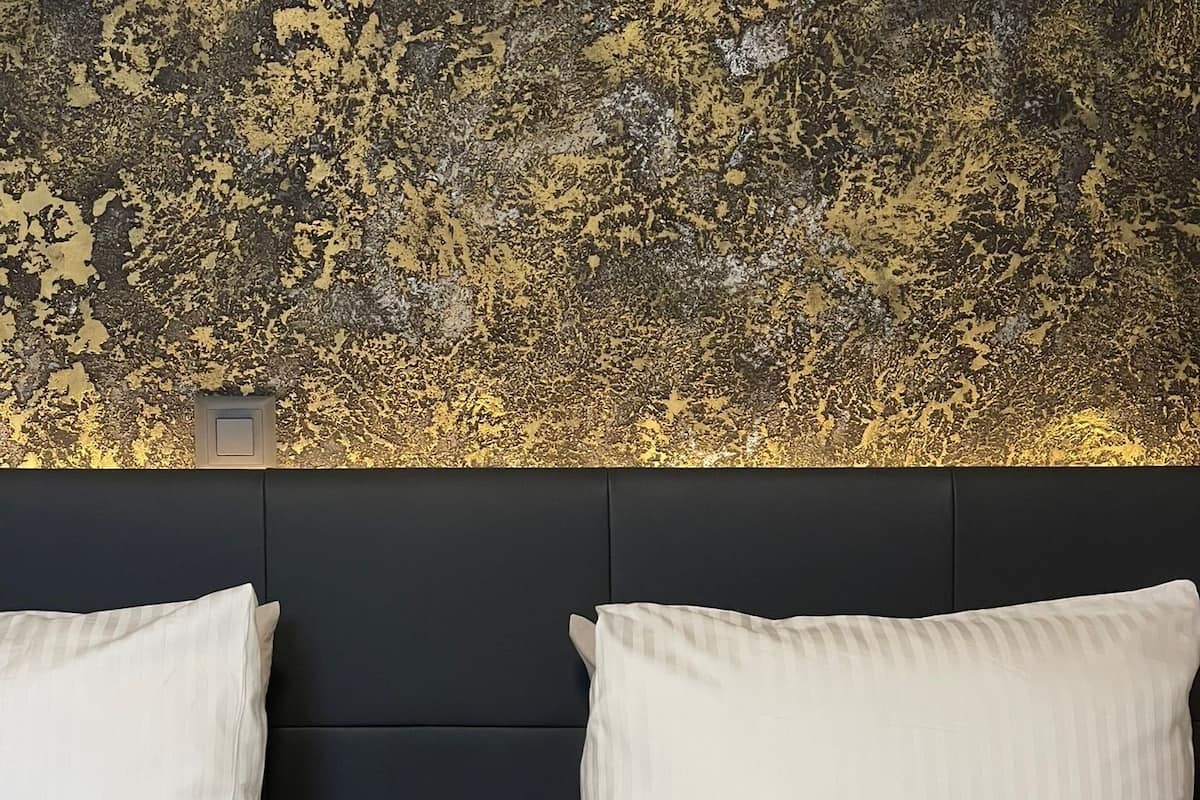 Een bed met twee kussens en een gestreept dekbed, voor een wand met textuur en een donkere hoofdbord.