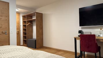 A bedroom with a bed, a wooden wardrobe, a desk with a chair, and a television.