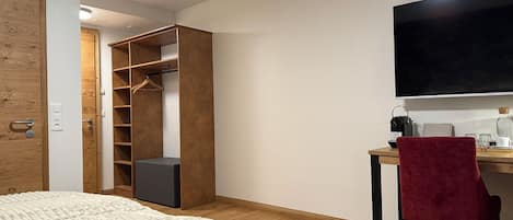 Quarto com cama, guarda-roupa de madeira, escrivaninha com cadeira e televisão.