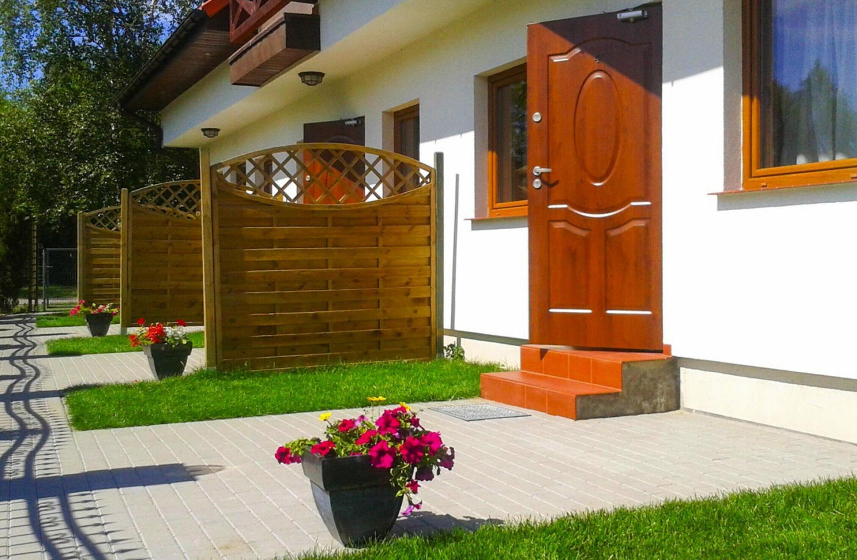 A house with a wooden gate, a red door, and a paved walkway with potted plants.