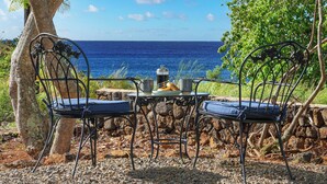 A table with two chairs, a metal table, and a view of the ocean. - Charming 3BR Koloa Shore Cottage with ocean views and AC, sleeps 6 in Poipu (Koloa)