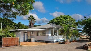 A single-story house with a porch, a fenced yard, and a gravel driveway. - Charming 3BR Koloa Shore Cottage with ocean views and AC, sleeps 6 in Poipu (Koloa)