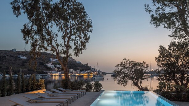 Una piscina con sillas de descanso, rodeada de árboles y con vistas a una masa de agua con edificios al fondo.