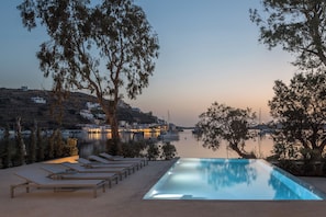 A swimming pool with lounge chairs, surrounded by trees and overlooking a body of water with buildings in the background. - Okeanos Kea (Vourkari)