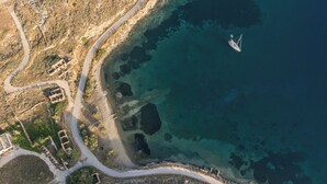 Vista aérea de una zona costera con una carretera despejada, terreno rocoso y un barco en el agua.
