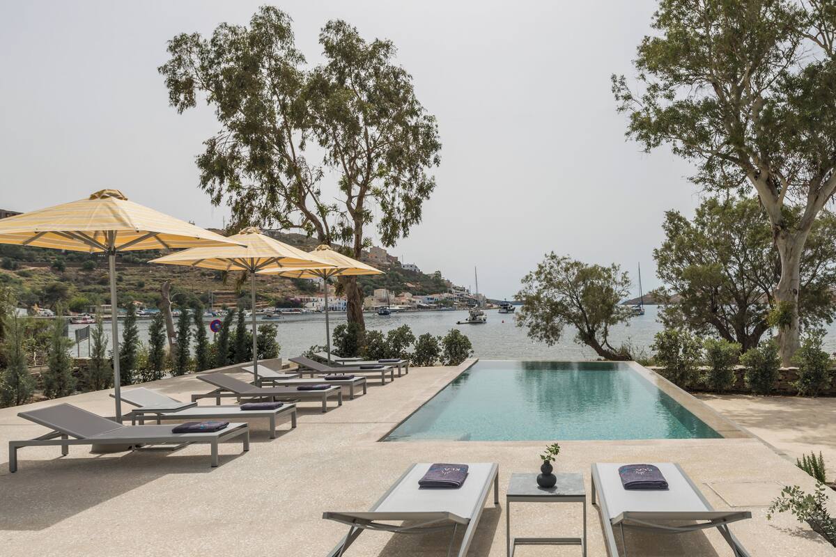 A poolside area with lounge chairs and umbrellas, overlooking a body of water with boats.