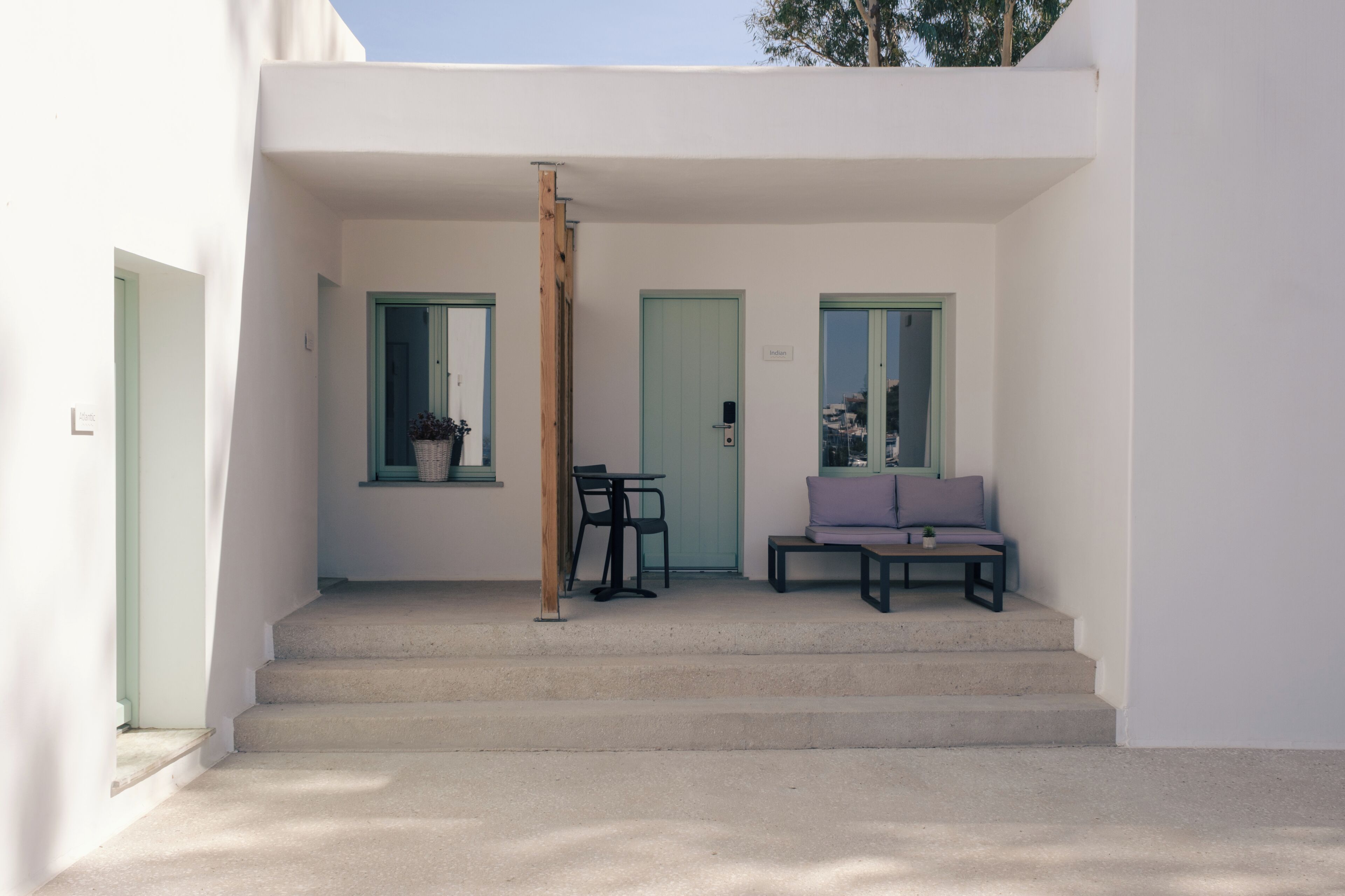 A modern building with a staircase leading to a covered entrance, a bench, and a table with chairs.