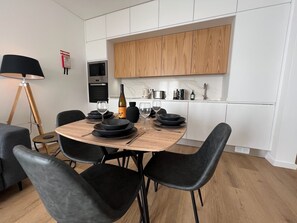 Una cocina moderna con armarios blancos, encimera de madera y un comedor con sillas negras y una mesa redonda.