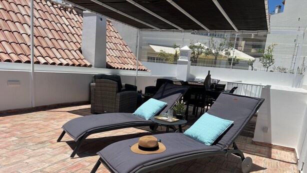 Eine Dachterrasse mit zwei Liegestühlen, einem kleinen Tisch und einem Korbstuhl.