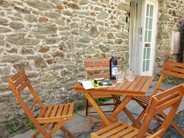 Un muro de piedra con una mesa y sillas de madera, una botella y vasos.