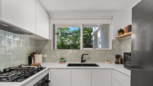 A modern kitchen with white cabinets, a gas stove, a sink, and a window overlooking greenery. - Stylish 2-bed Townhouse in Leafy Hyde Park (Adelaide)
