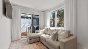 A modern living room with a beige sectional sofa, a patterned rug, and large windows with white curtains. - Stylish 2-bed Townhouse in Leafy Hyde Park (Adelaide)