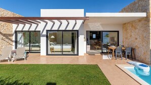 Ein modernes Haus mit Pool, Terrasse und durch Glastüren einsehbarer Küche.
