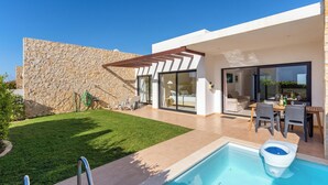 Ein modernes Haus mit Swimmingpool, einer Steinmauer und einer Terrasse mit Gartenmöbeln.