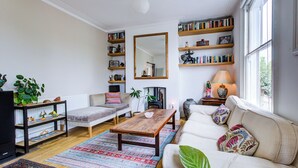 A living room with a sofa, coffee table, and bookshelves. - Charming Three Floor Retreat in Lower Clapton with Friendly Cats and Nature (London)