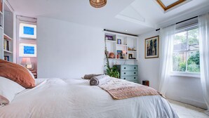 A bedroom with a large bed, a built-in bookshelf, a dresser, and a window with curtains. - Charming Three Floor Retreat in Lower Clapton with Friendly Cats and Nature (London)