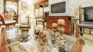 Ein wohnzimmer im Vintage-Stil mit antiken Möbeln, einem Glastisch mit Dekorationen und einer Steinwand.