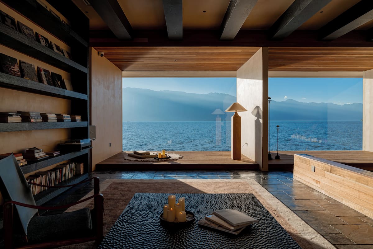 A modern interior with a view of the sea, a bookshelf, a seating area, and a lamp.
