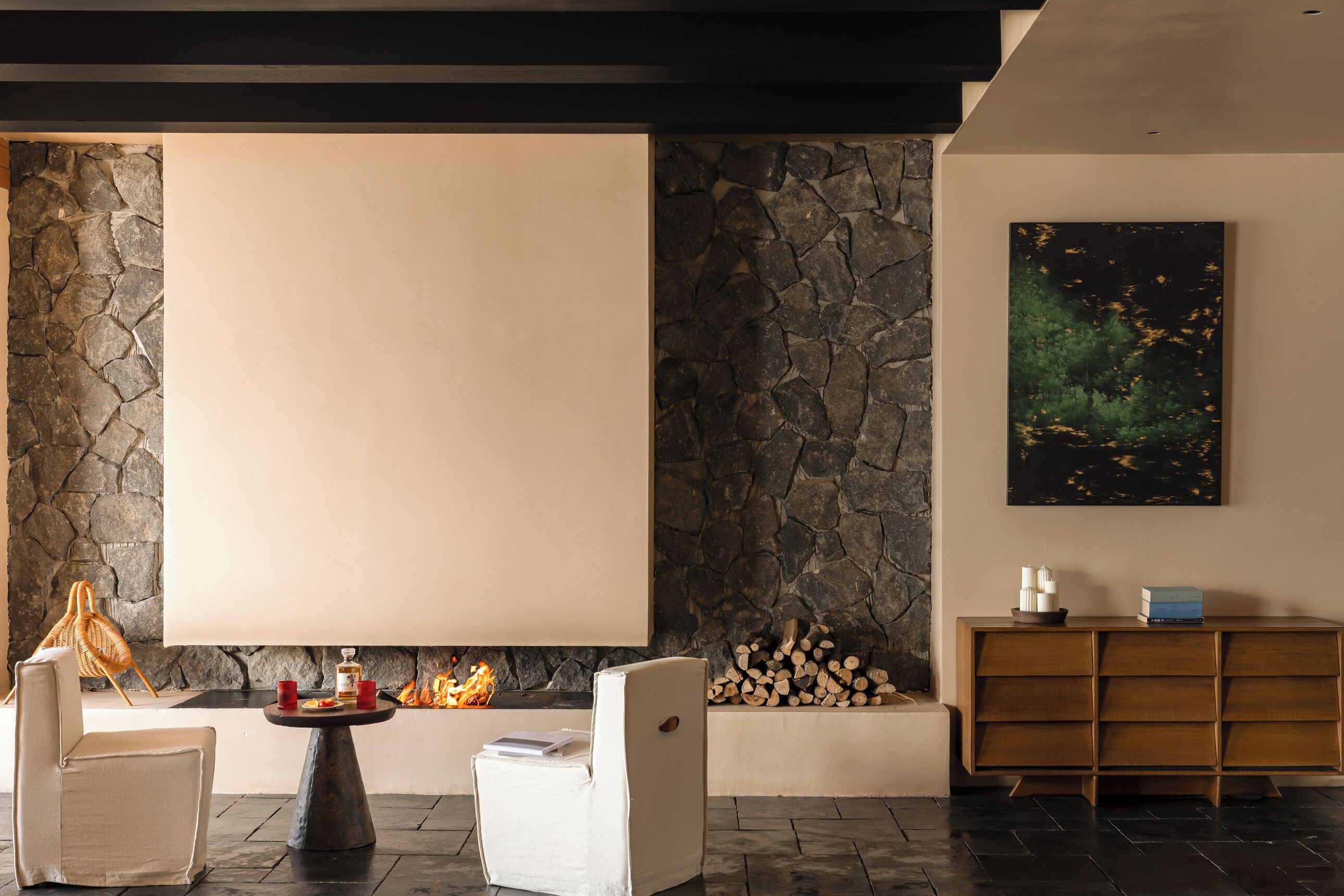 A modern living room with stone walls, a fireplace, a large window, and a minimalist wooden cabinet.