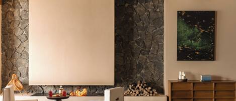 A modern living room with stone walls, a fireplace, a large window, and a minimalist wooden cabinet.